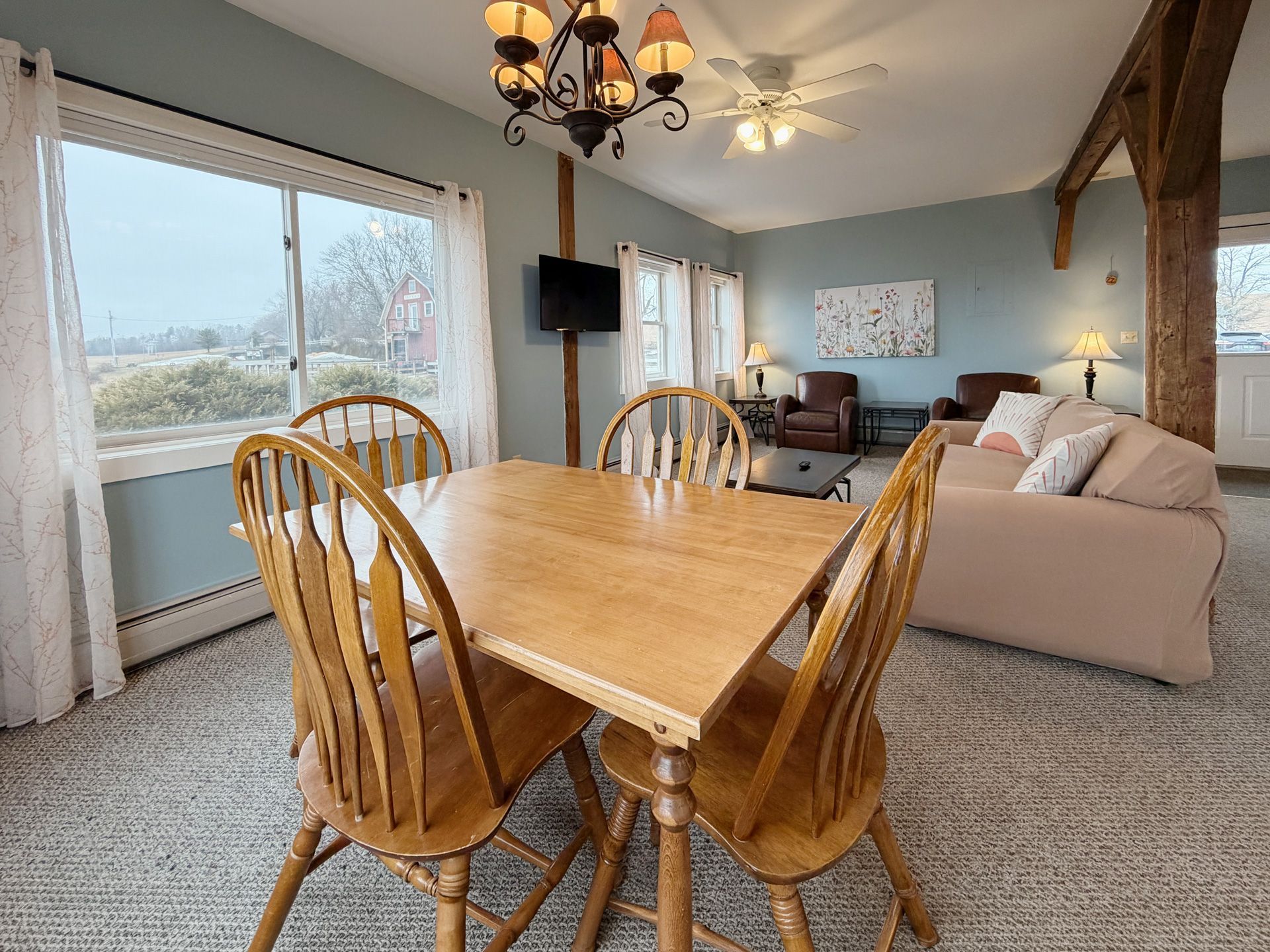 Dining and living room with wooden table, beige sofa, TV, and large windows overlooking water
