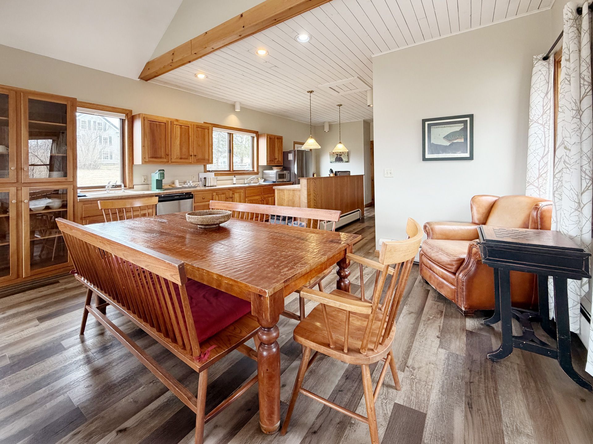 Open-plan kitchen and dining area with wood table, bar stools, sofa, and large windows