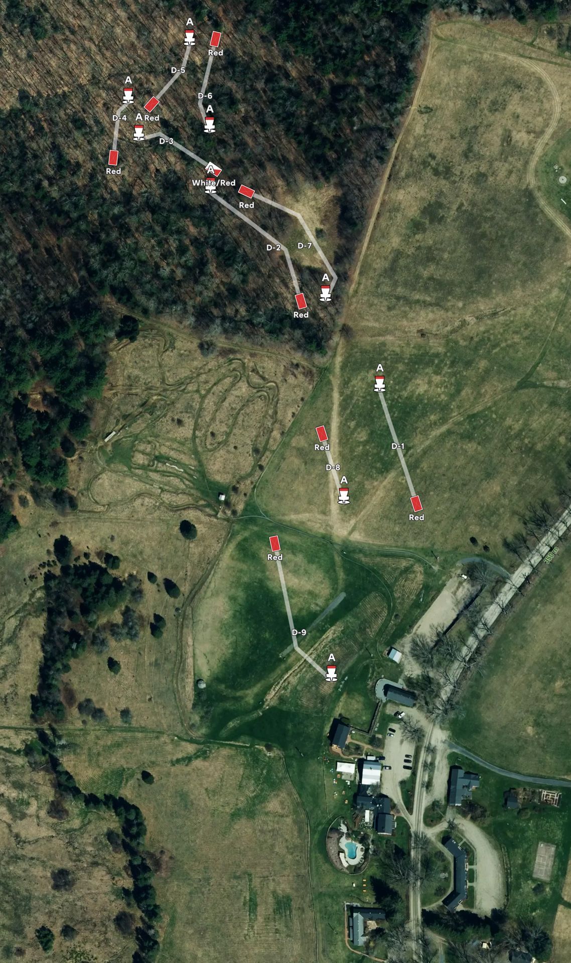 Aerial view of a wooded hillside and fields with a marked trail and several red route markers.
