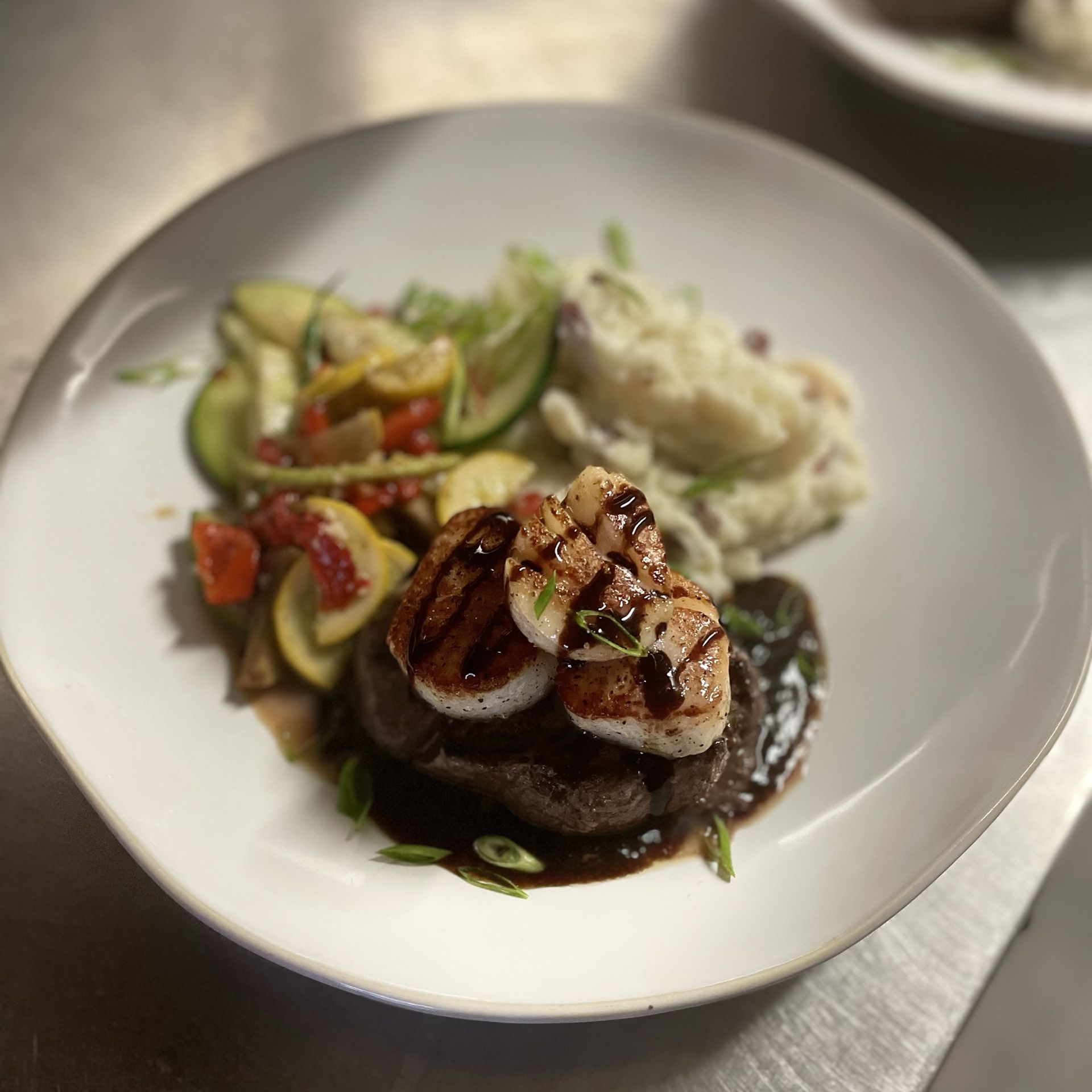 Plated gourmet meal with steak, vegetables, and mashed potatoes on a white dish