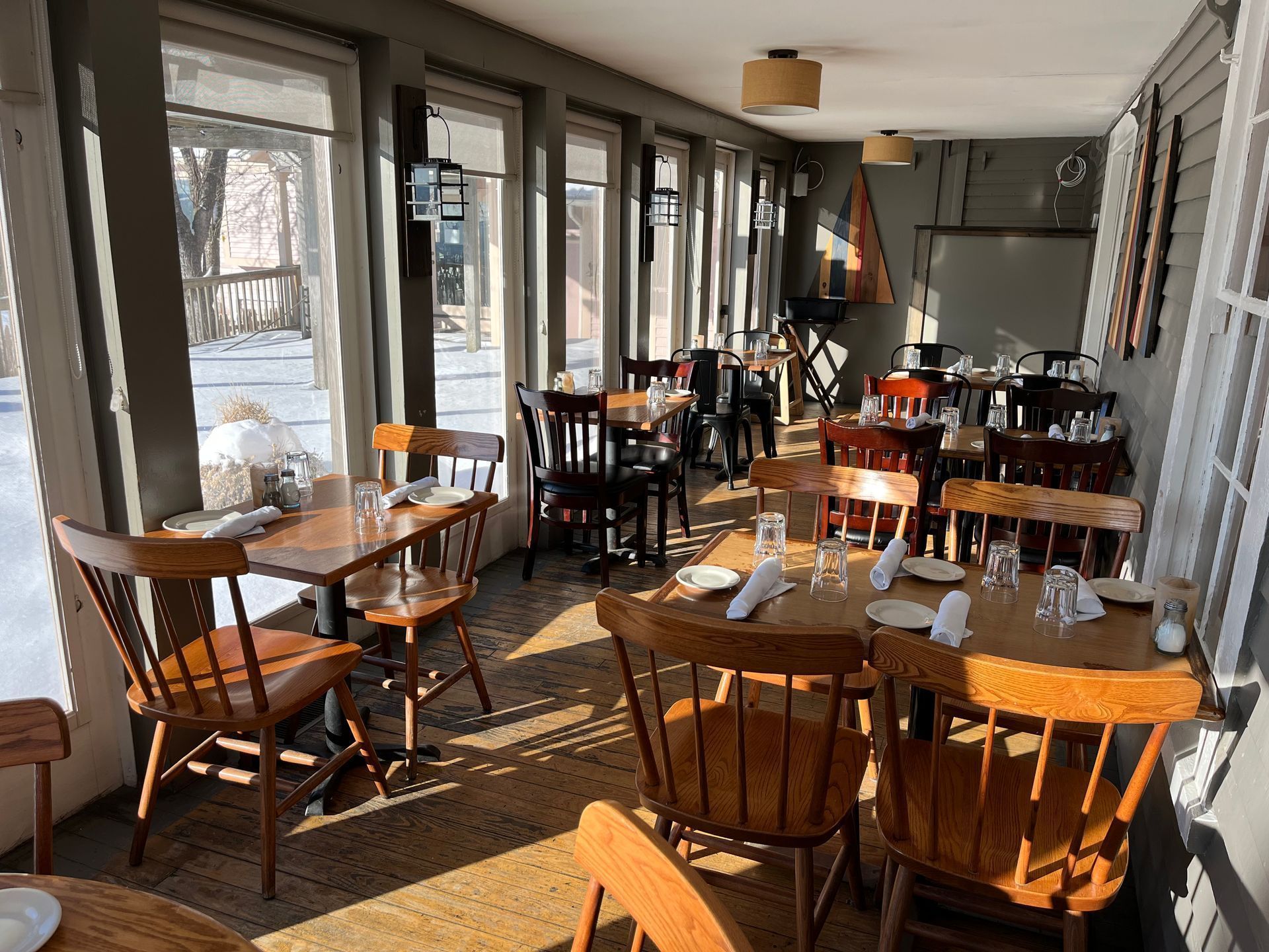 Sunlit café dining area with wooden tables and chairs along large windows
