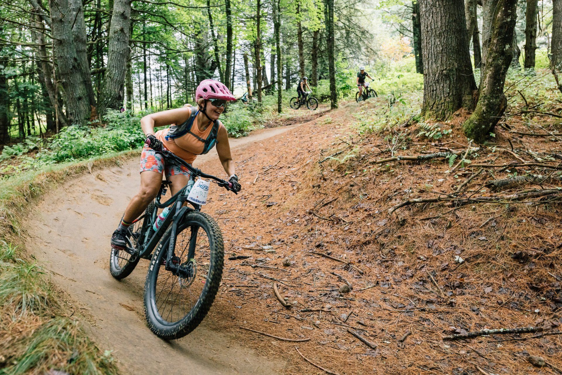 Mountain biker in a pink helmet riding a forest trail through tall trees