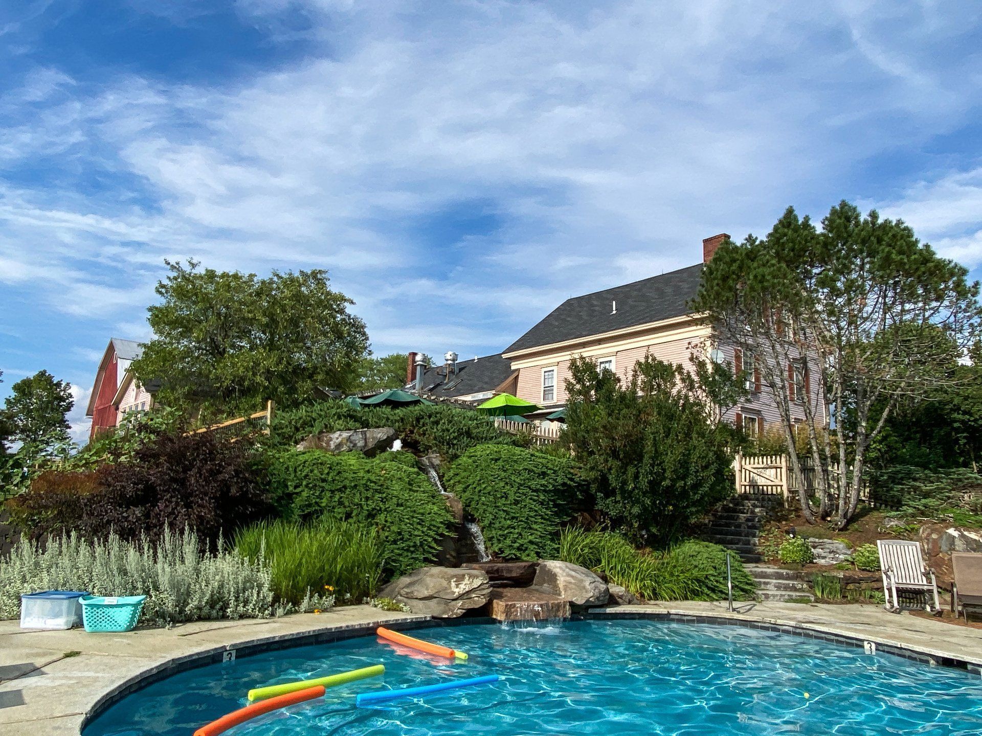 Backyard swimming pool beside a landscaped garden and house under a blue sky