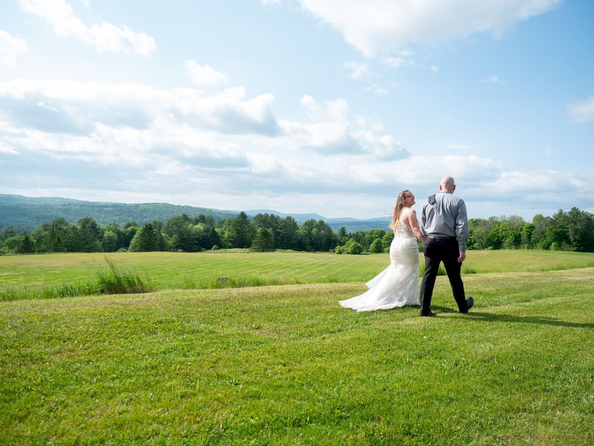Bride and groom standing in a green field under a bright blue sky