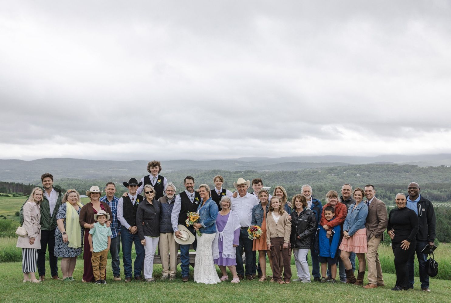 Group of people standing together outdoors on a grassy hill under a cloudy sky.
