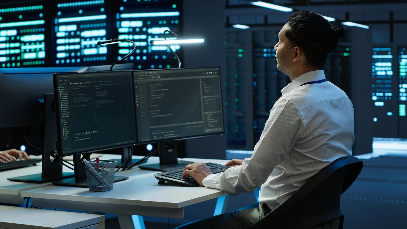 A man is sitting at a desk in front of three computer monitors.