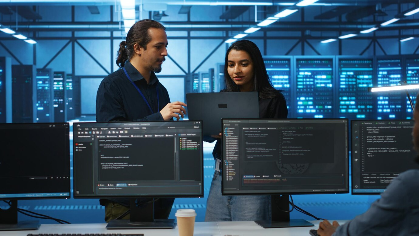 A man and a woman are looking at a laptop in a server room.