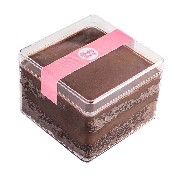 Chocolate cake in a clear square container, sealed with a pink band. The cake has multiple visible layers.