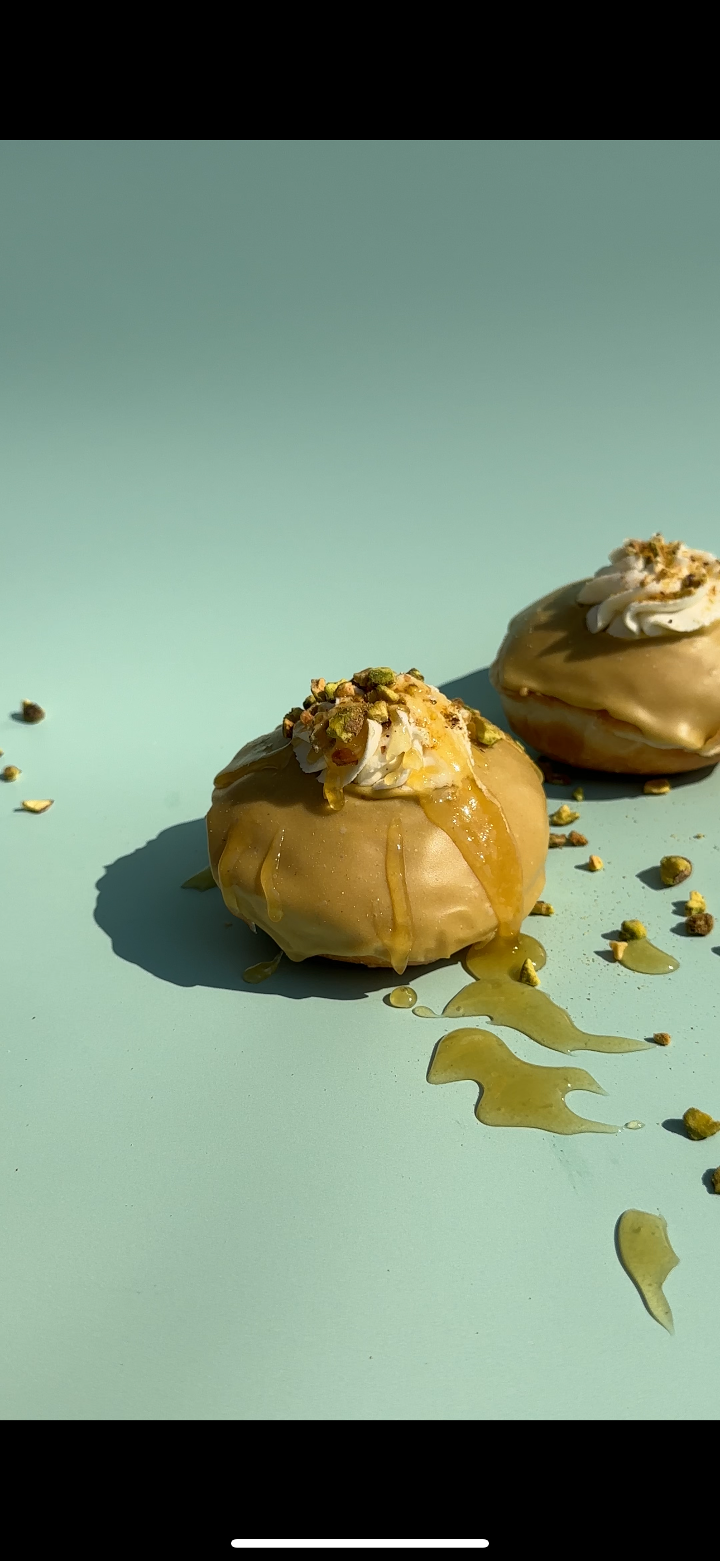 Two golden-glazed pastries on a light blue surface, drizzled with a golden sauce and sprinkled with crumbs.