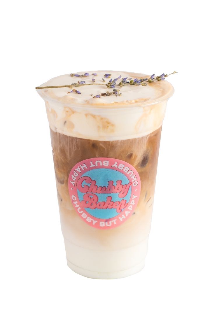 Iced lavender latte in a clear plastic cup with a pink and blue logo, topped with foam and lavender sprigs.