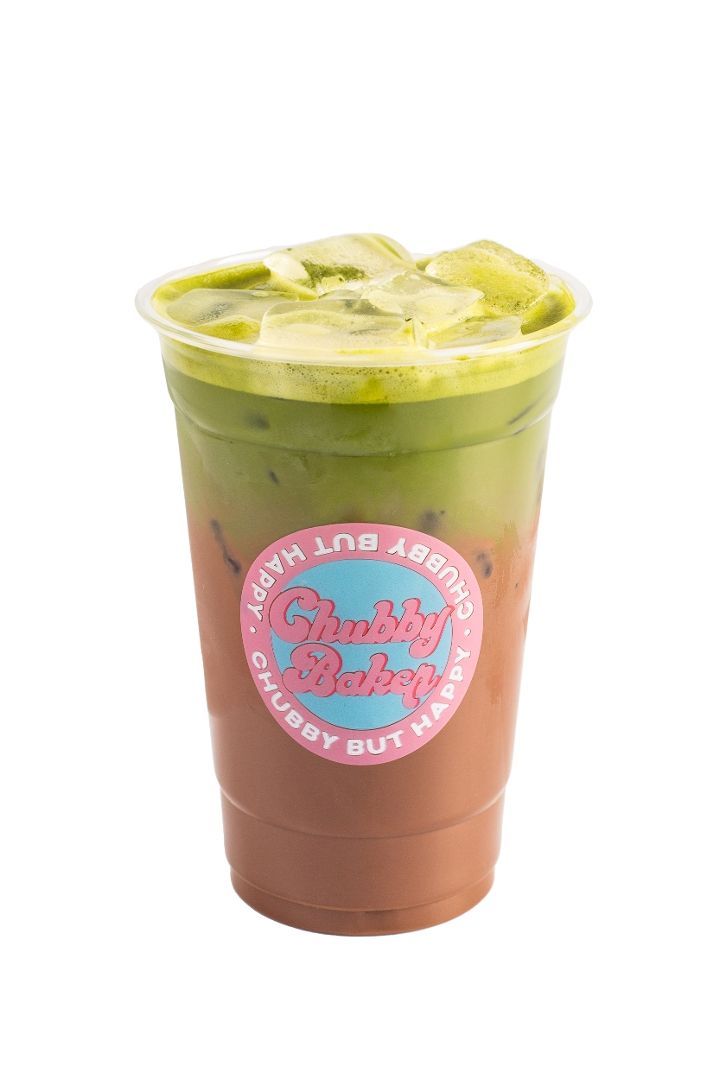 Iced matcha latte with three distinct layers, visible through the clear cup. The layers are green, light brown, and dark brown. Pink shop logo is on the cup.