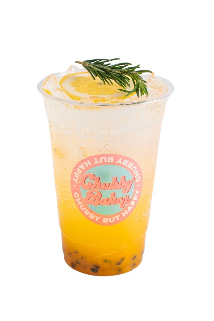 A passionfruit soda in a clear plastic cup, garnished with an orange slice and rosemary. The cup has a pink and white logo that reads 