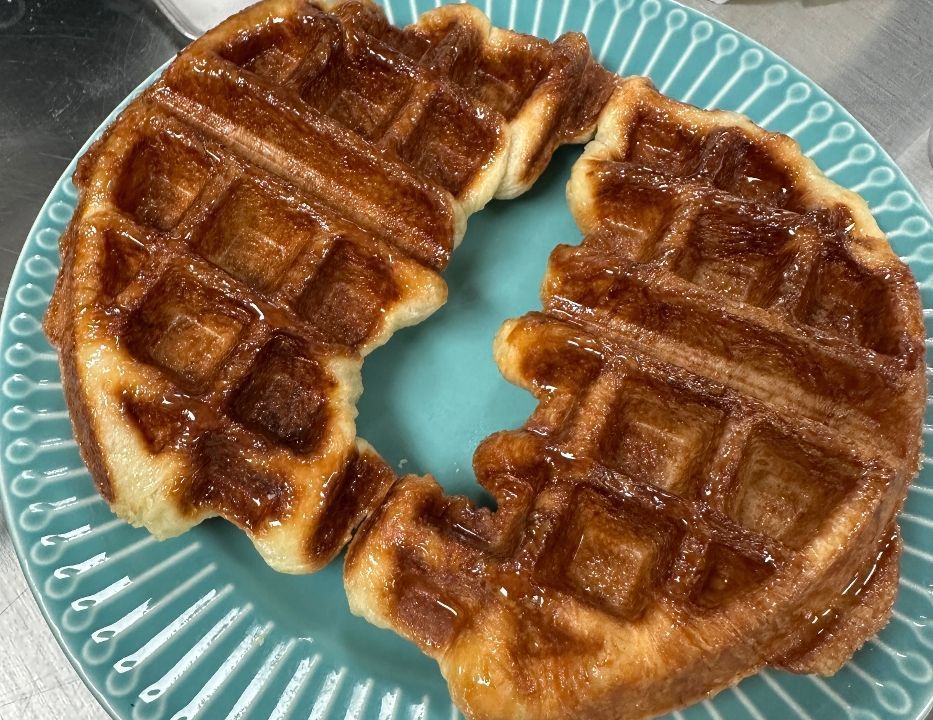 Two golden-brown waffles on a teal plate, drizzled with syrup.