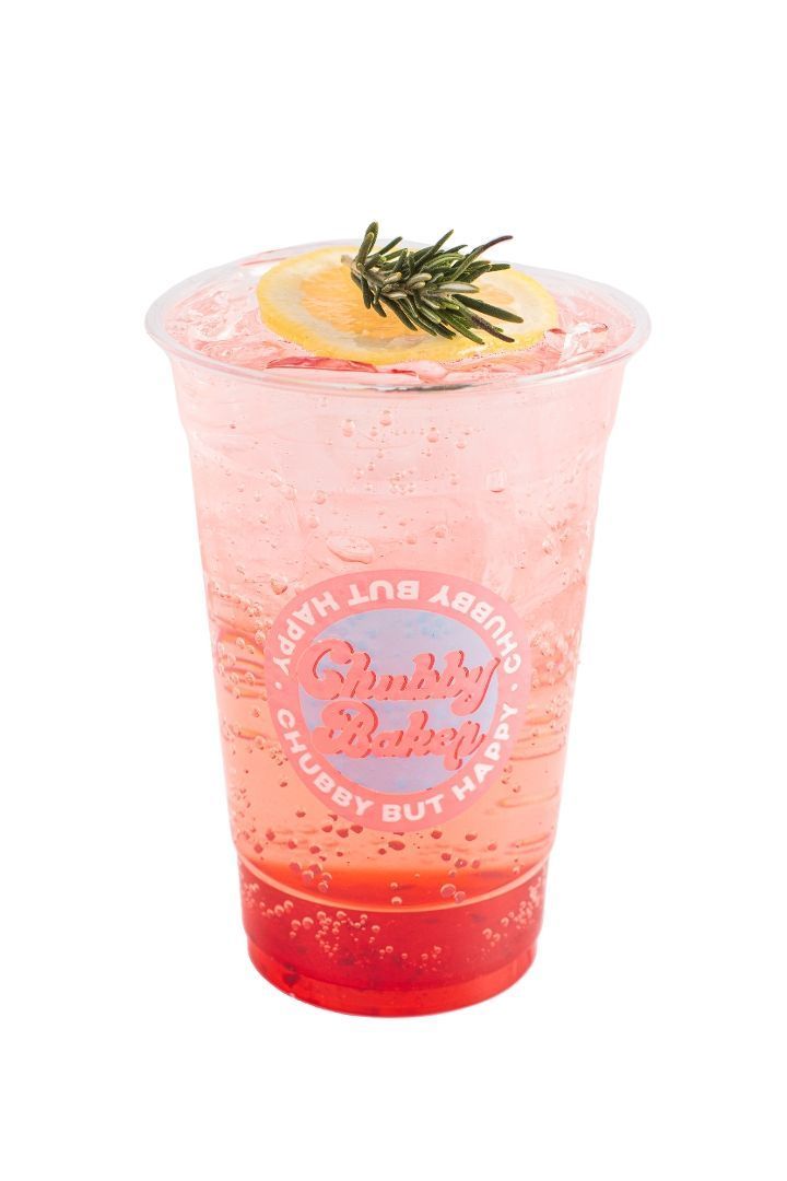 A clear plastic cup of pink bubbly drink with a lemon slice and rosemary garnish. The cup has a logo that reads 