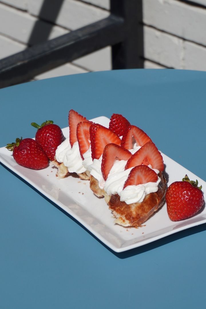 Strawberry dessert with whipped cream on a rectangular white plate, garnished with fresh strawberries, placed on a blue table.