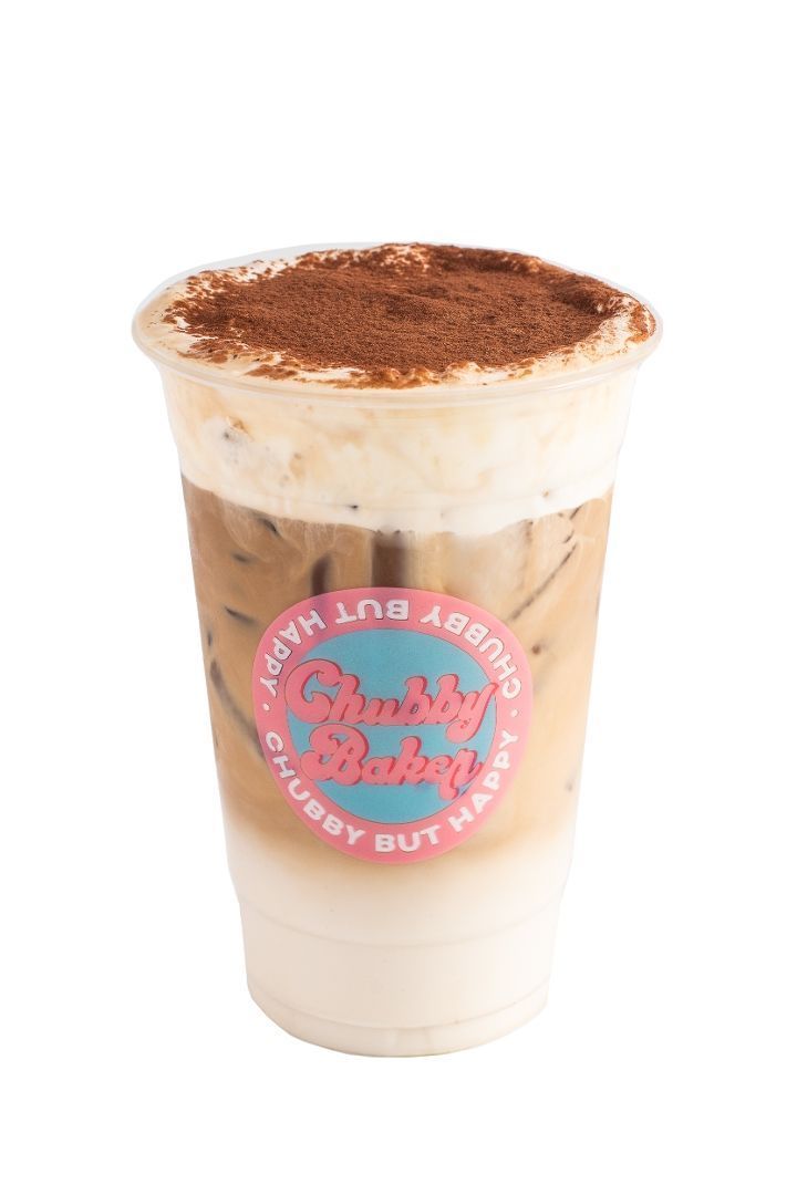 Iced coffee drink with a whipped topping dusted with cocoa powder, in a plastic cup with a logo.