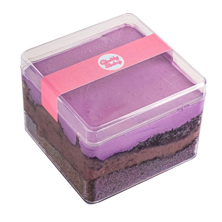 Square cake in a clear plastic container, layered with purple frosting and chocolate cake; pink band with logo.