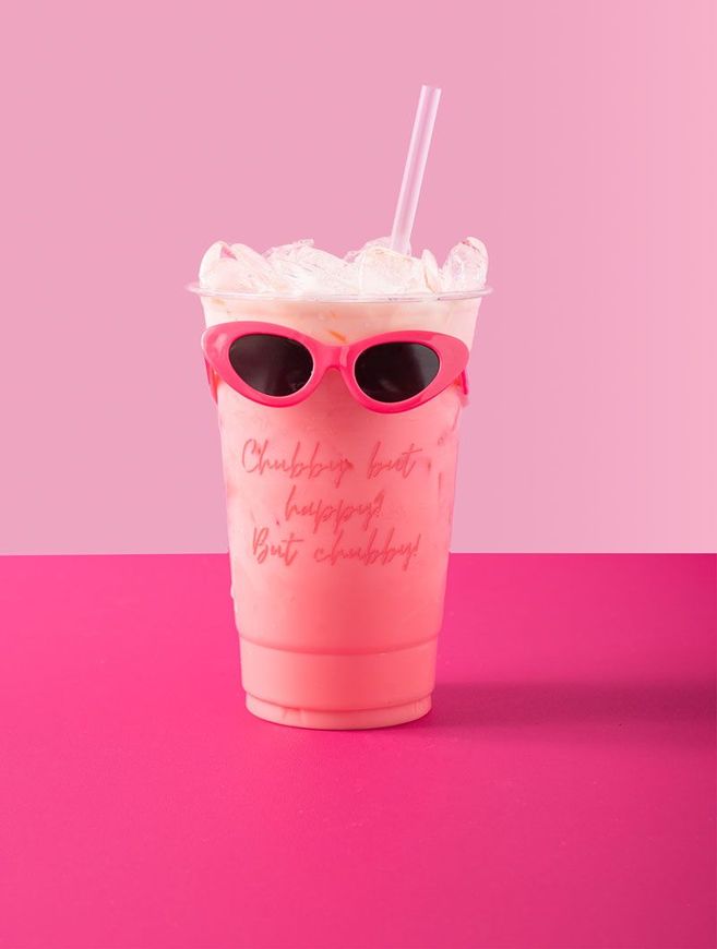 Pink drink in a clear cup with sunglasses, a straw, and ice, set against a pink background.  Text on the cup reads 
