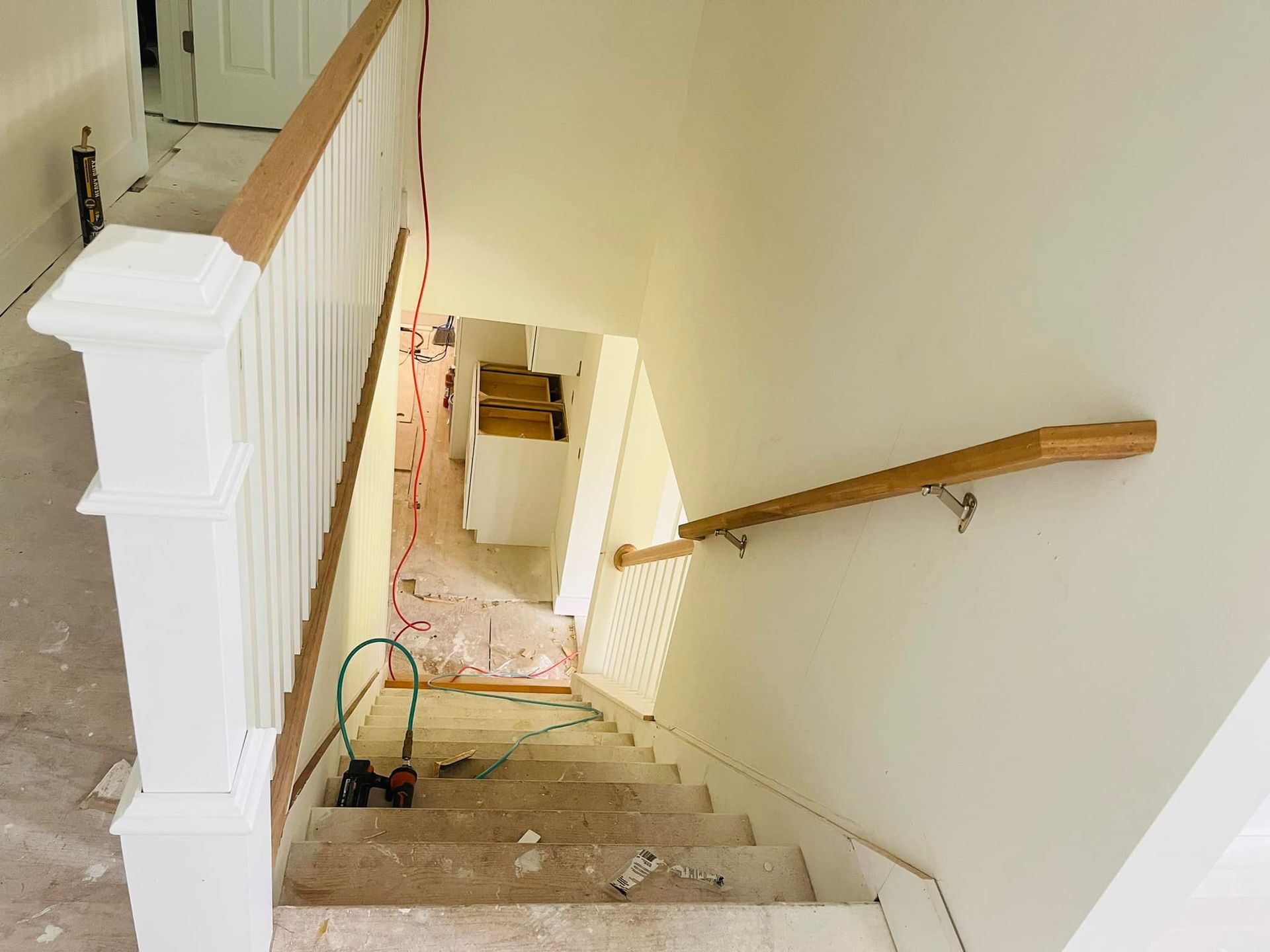 Staircase with oak handrails and white balusters. Stairwell with drywall and wood construction materials visible.