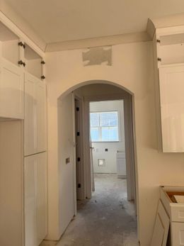 Kitchen hallway with white cabinets, archway, and unfinished walls.