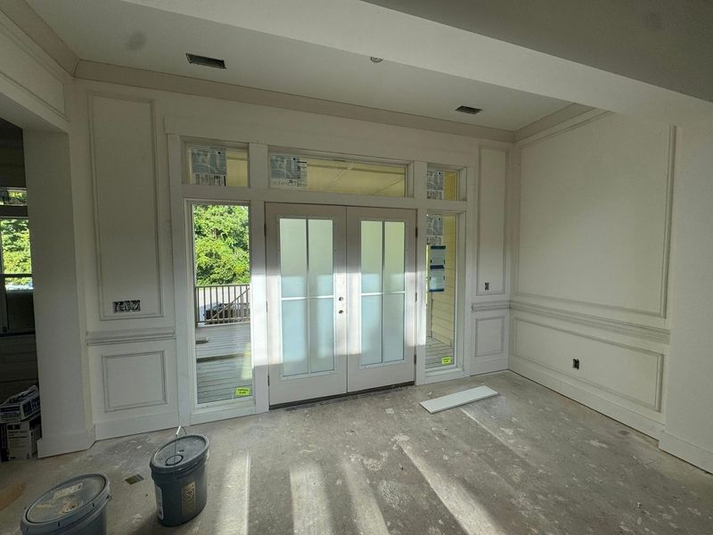 Interior view of a room with white paneled doors and walls, sunlight streaming through, and construction materials visible.