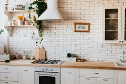 White kitchen with brick wall, stove, cabinets, and decorative plants.