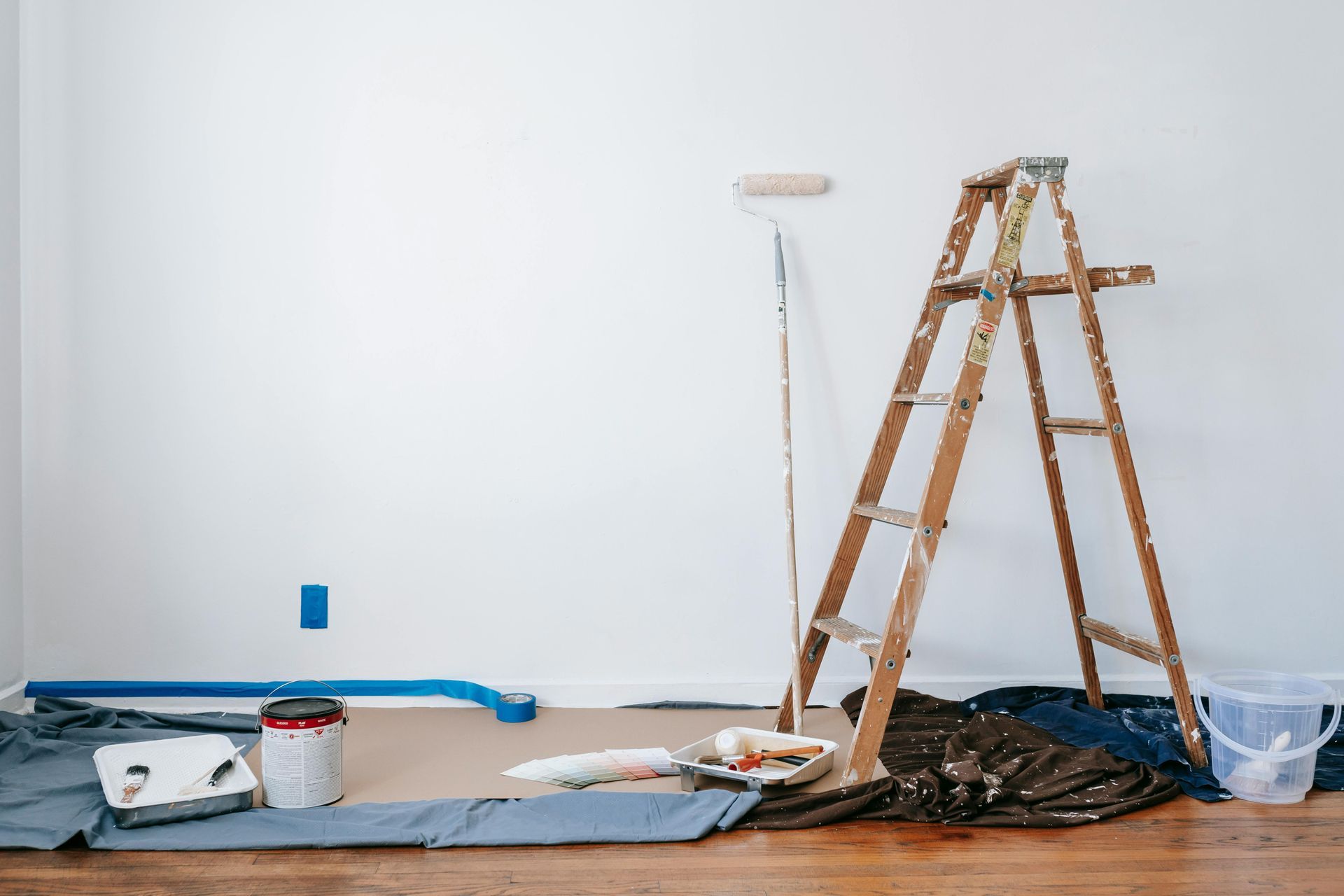 Ladder and paint supplies set up in a room with a white wall, ready for painting.