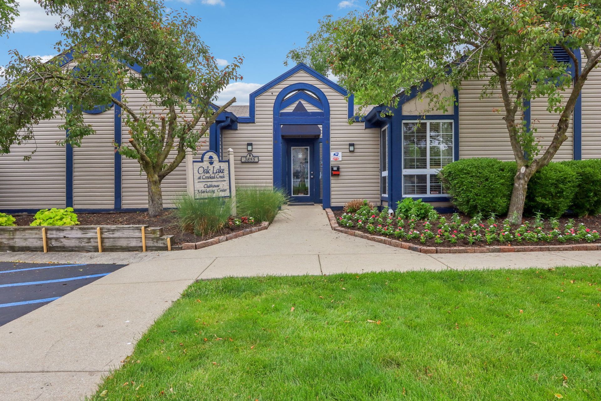 Apartment building entrance with a path, sign, and landscaping. Blue and beige exterior, trees, and green grass.