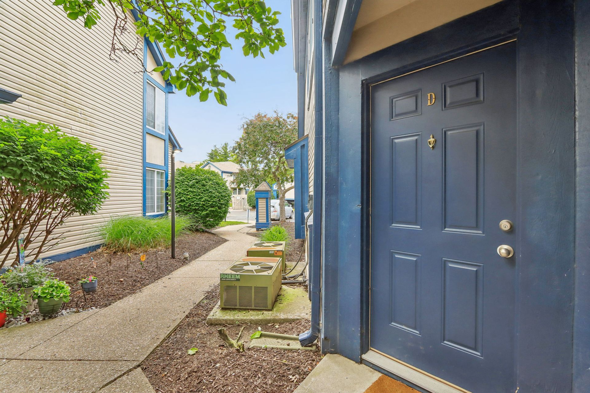 Blue door of a townhouse. Pathway leads toward building with bushes.