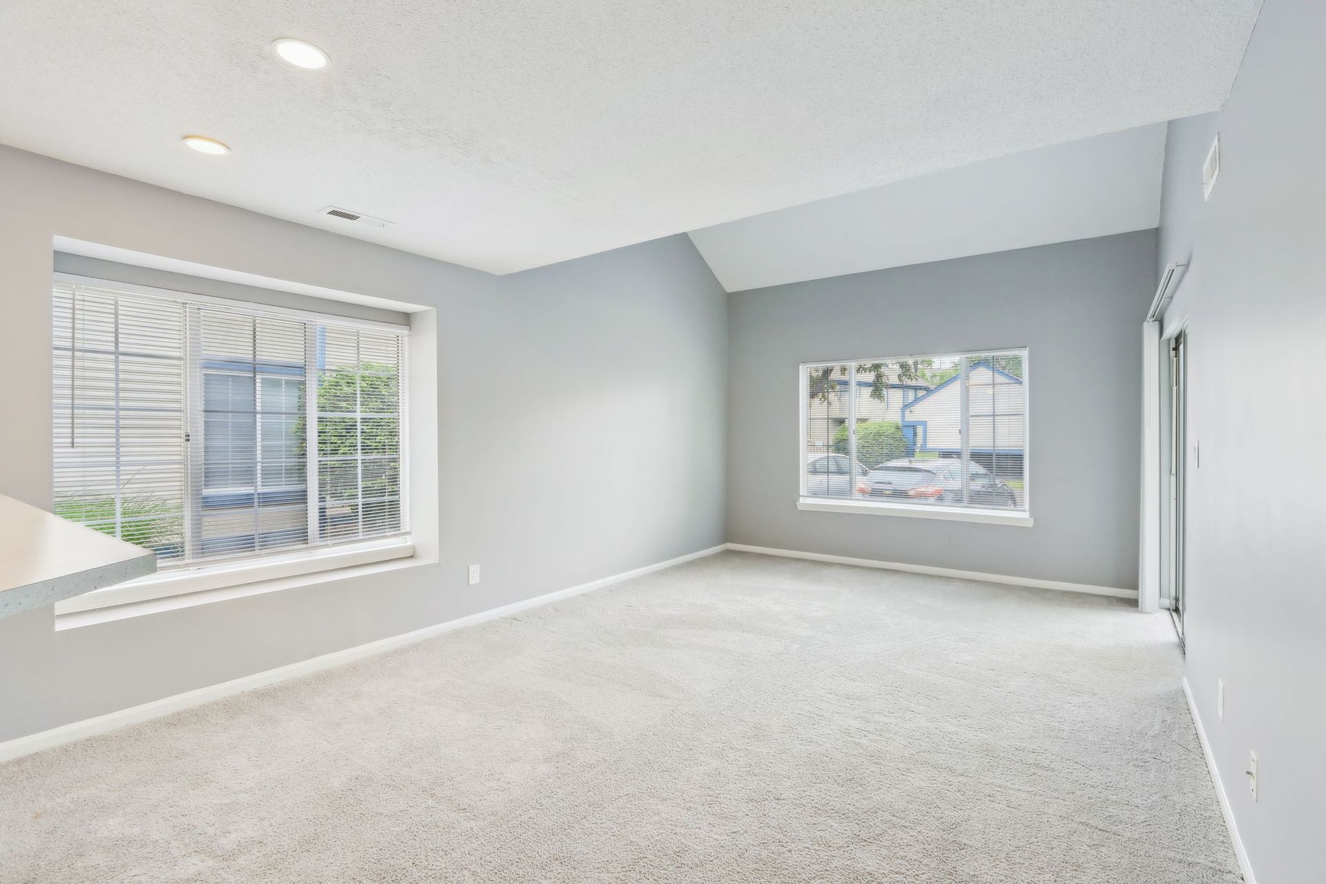 Empty living room with gray walls, light carpet, and two windows.