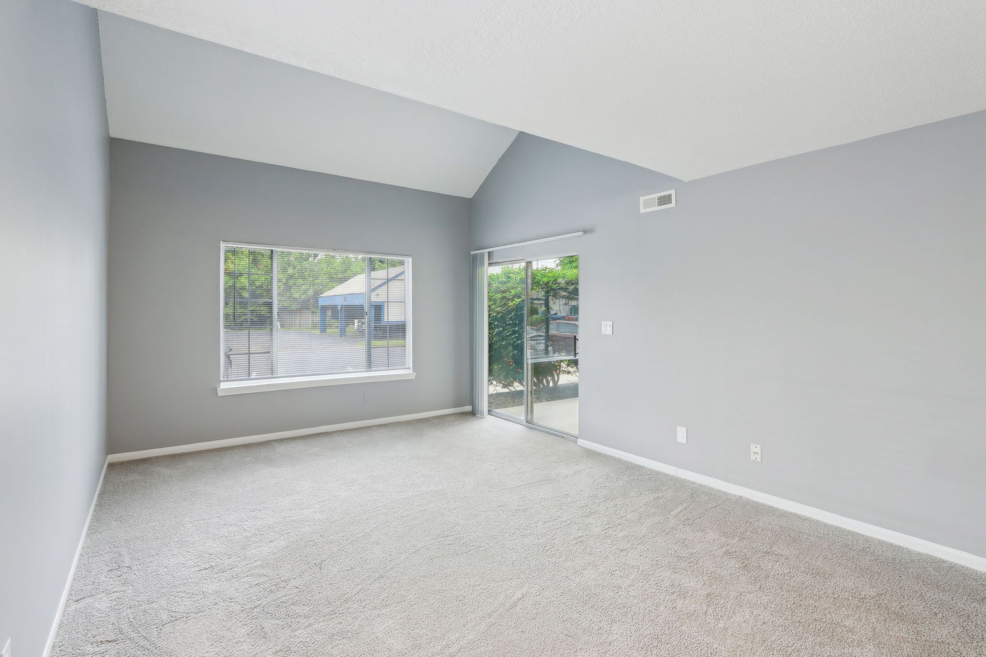 Empty room with gray walls, carpet, window, and sliding glass door to the outside.