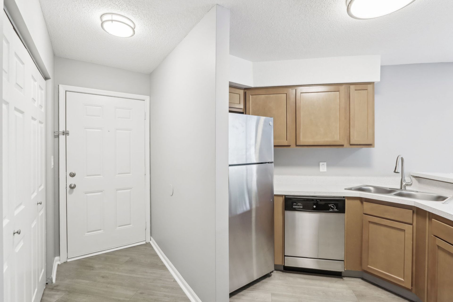Hallway entrance to kitchen with white door, cabinets, and stainless steel appliances.