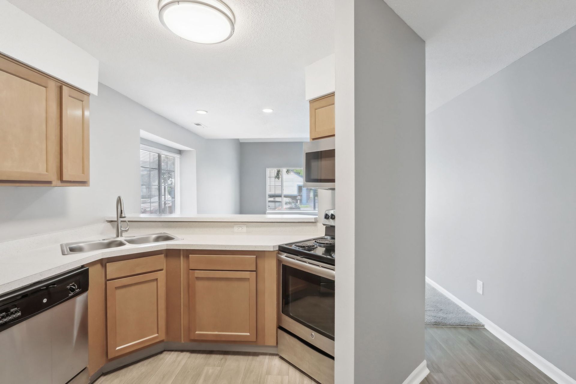 Kitchen with light wood cabinets, stainless steel appliances, and a view into a living area.