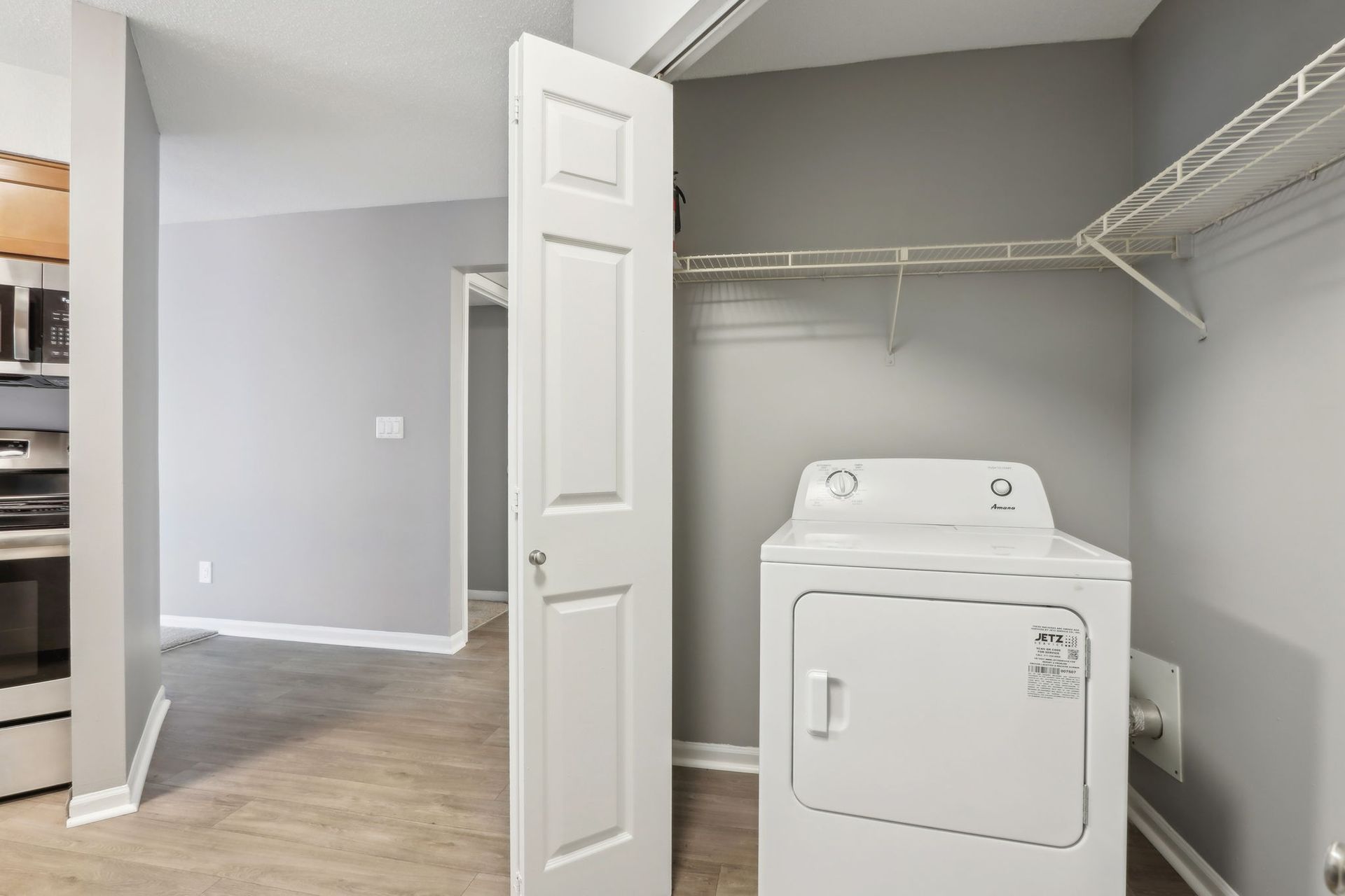 A laundry room with a white dryer, clothes rack, and open door to another room, with gray walls.