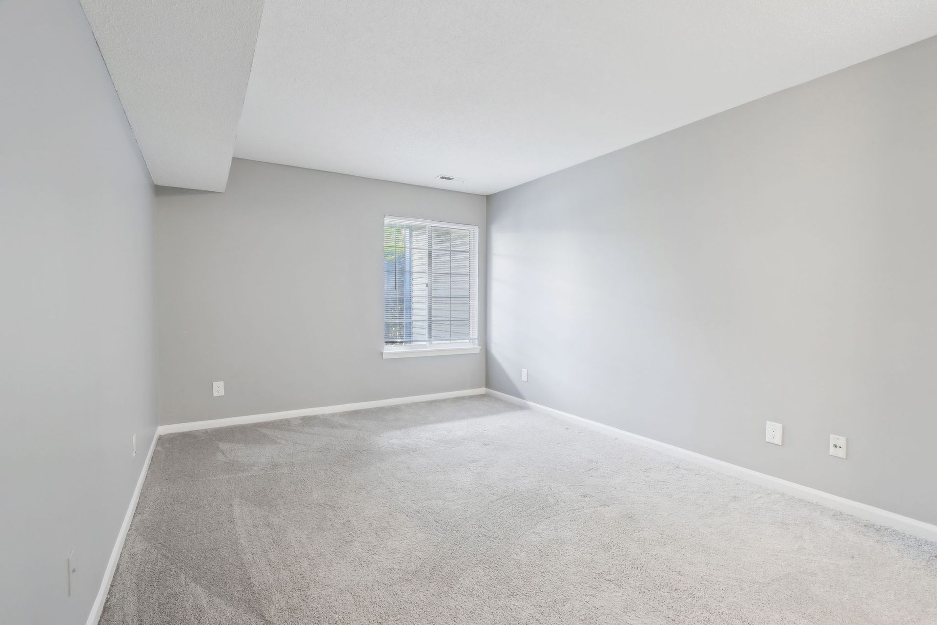 Empty bedroom with gray walls and carpet, a window, and light-colored ceiling.