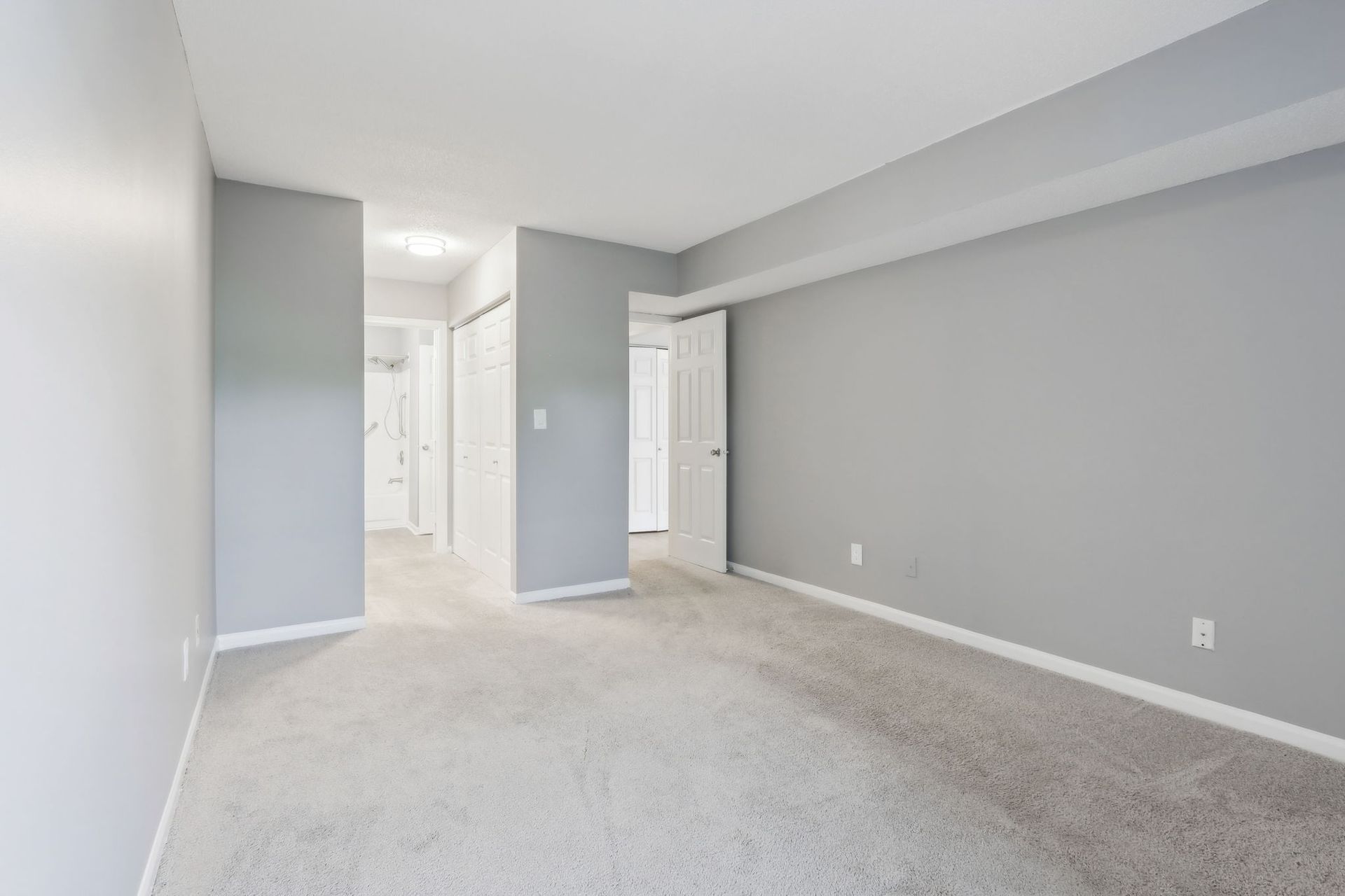 Empty room with gray walls, light carpet, and white doors leading to other rooms.