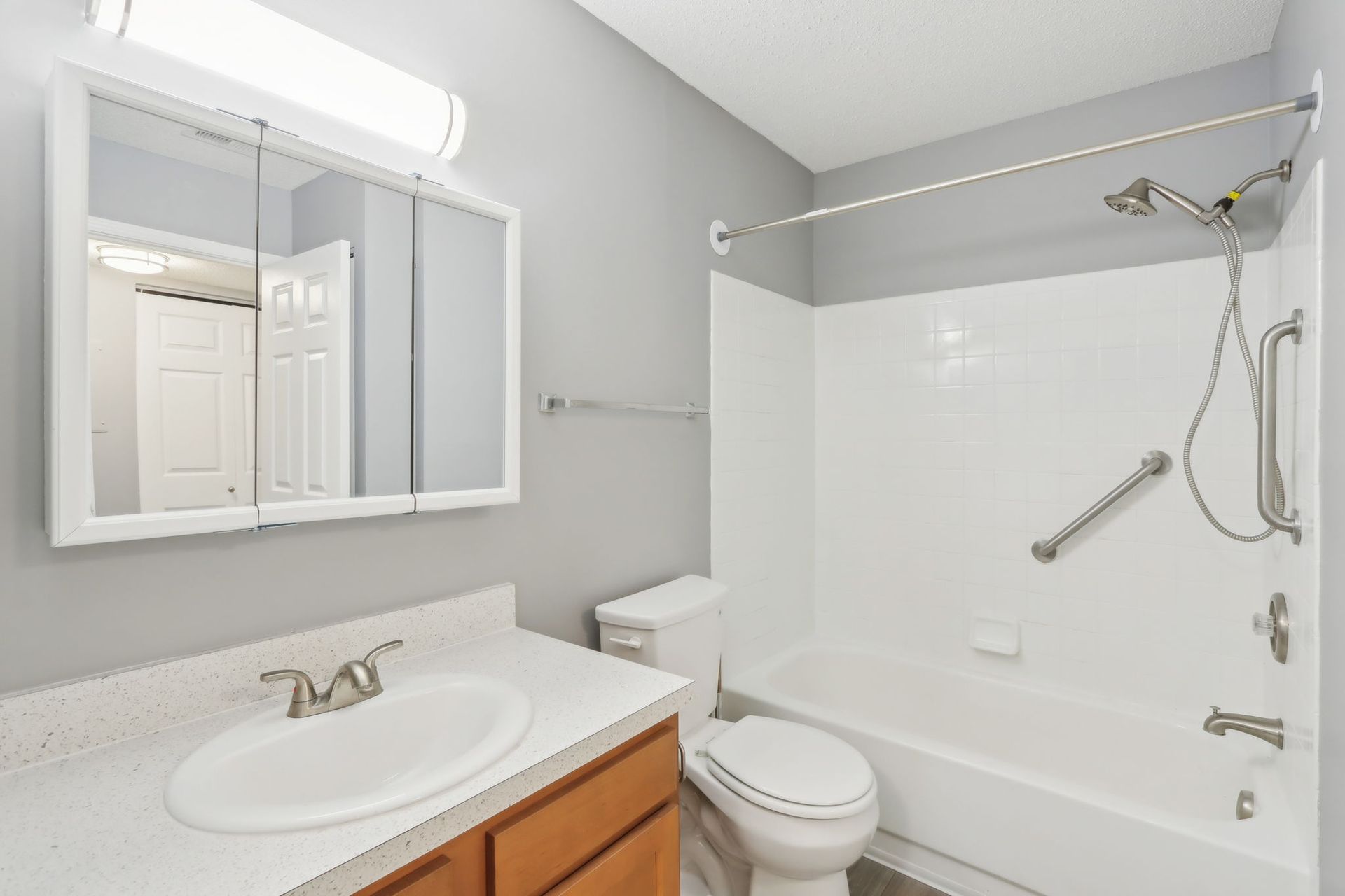 Bathroom with white fixtures, gray walls, and a brown vanity. Includes a tub/shower, toilet, and mirror.
