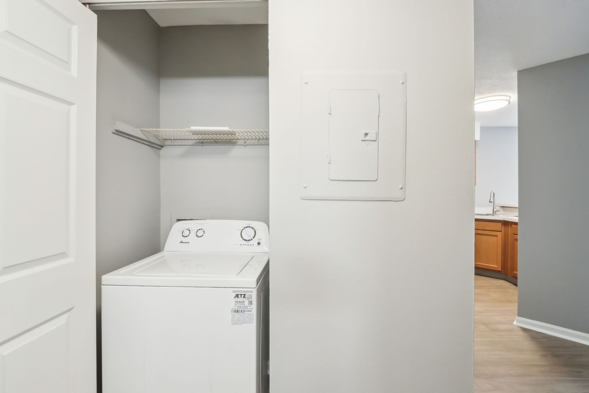 Laundry room with a white washing machine, shelf, and electrical panel on a grey wall.