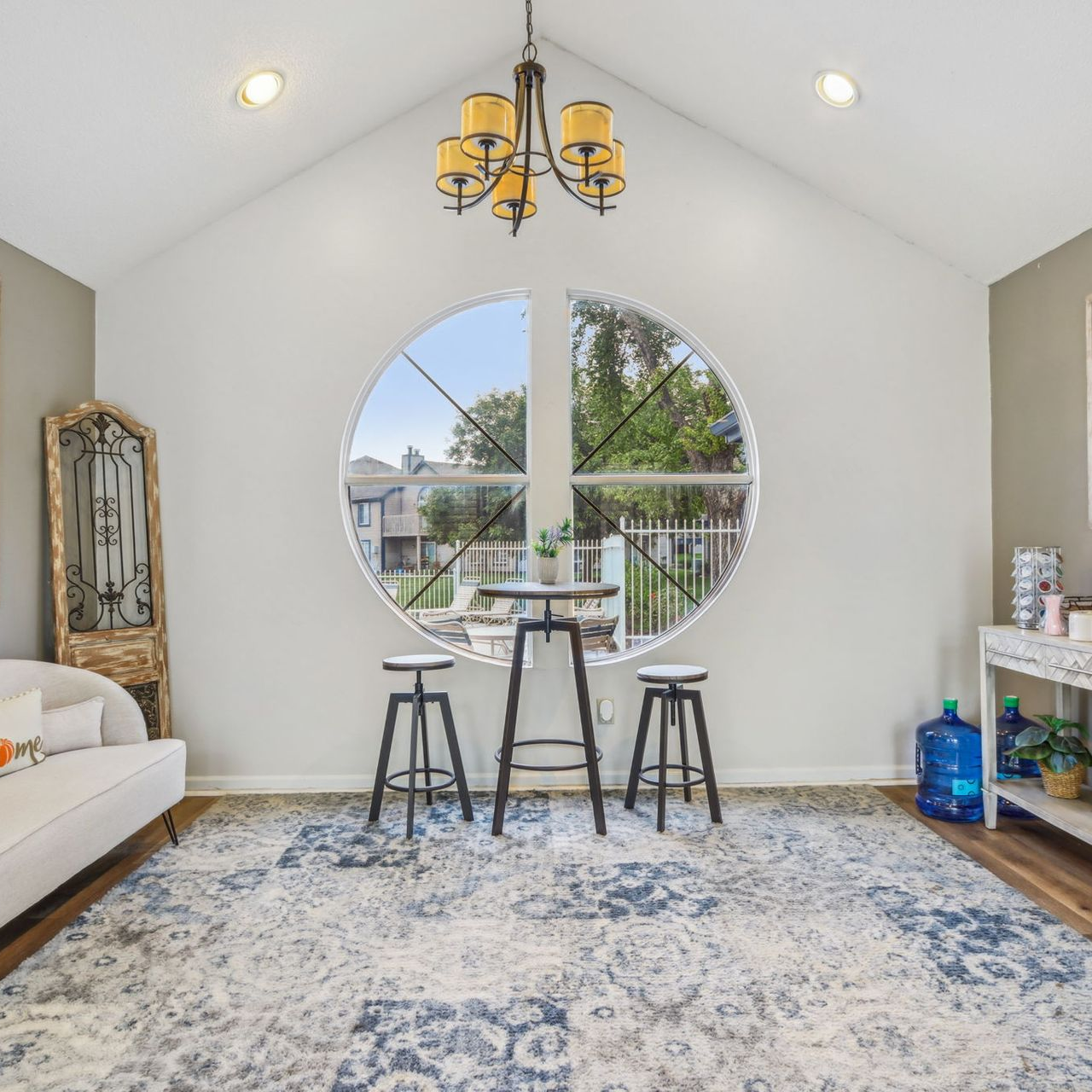Living room with large round window, rug, and table with stools. Includes a sofa and plants.