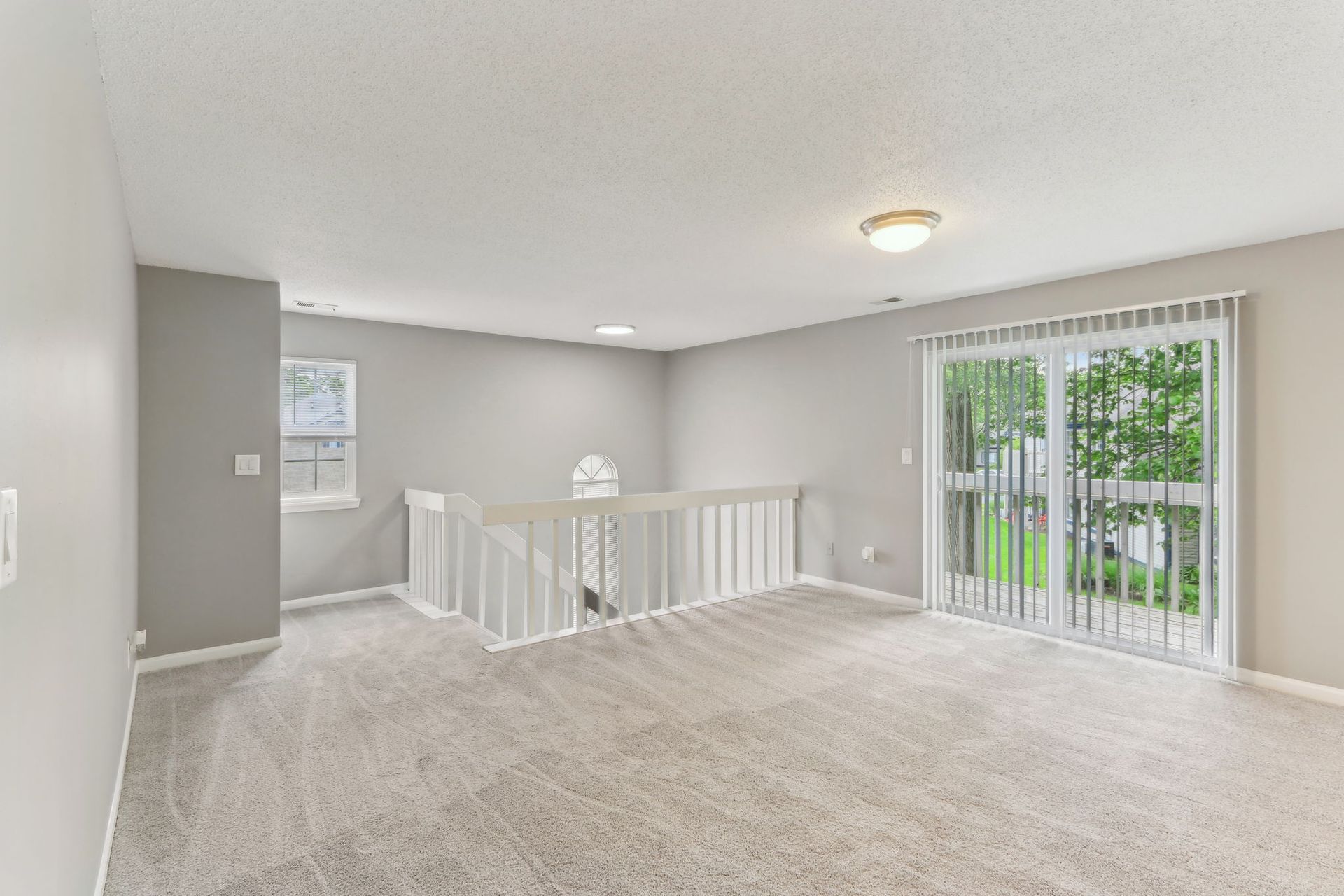 Open-concept loft with light gray walls, white railing, carpet, and sliding glass door to a green yard.