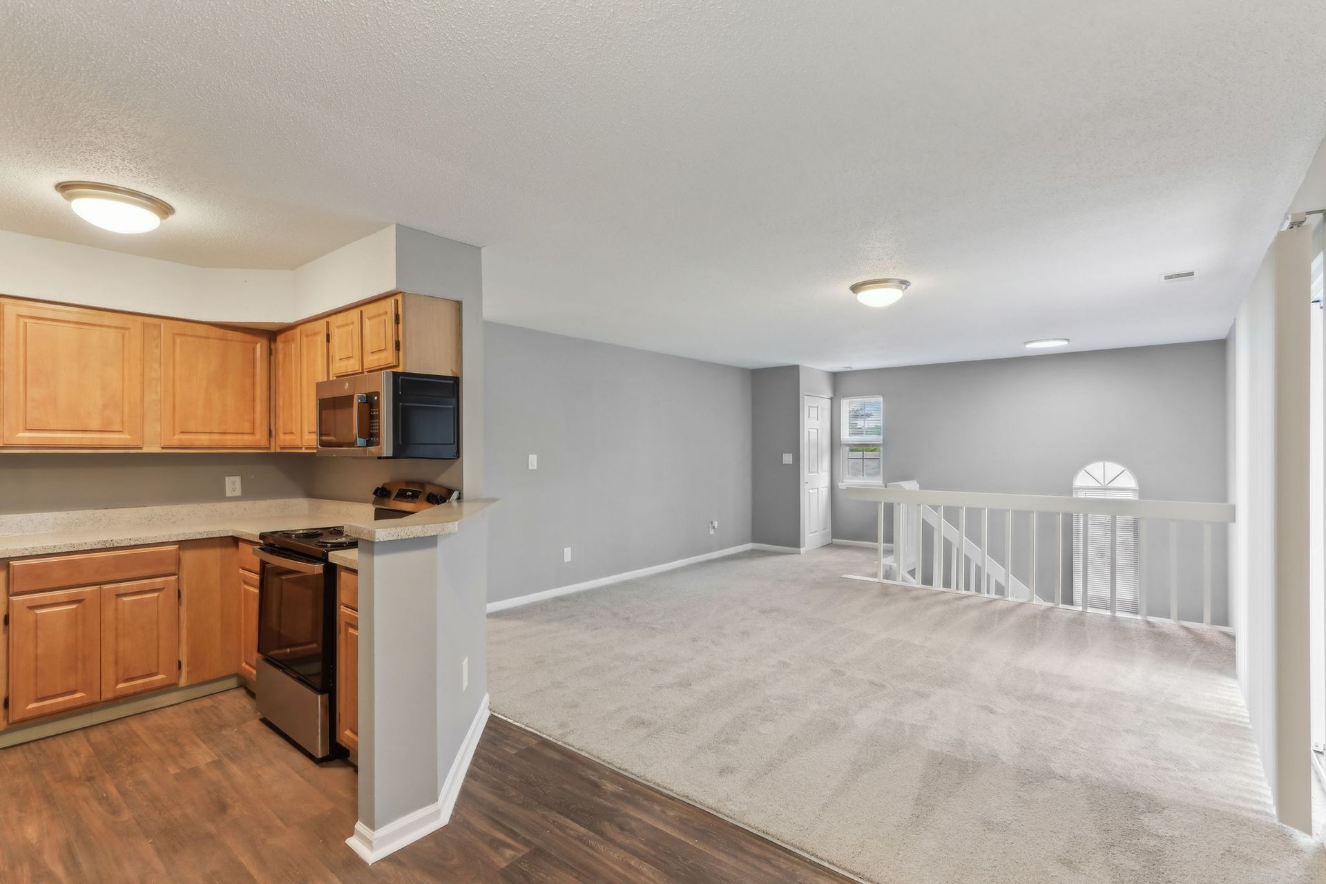 Kitchen area with wooden cabinets and stainless steel appliances, leading into a carpeted living space with a staircase.