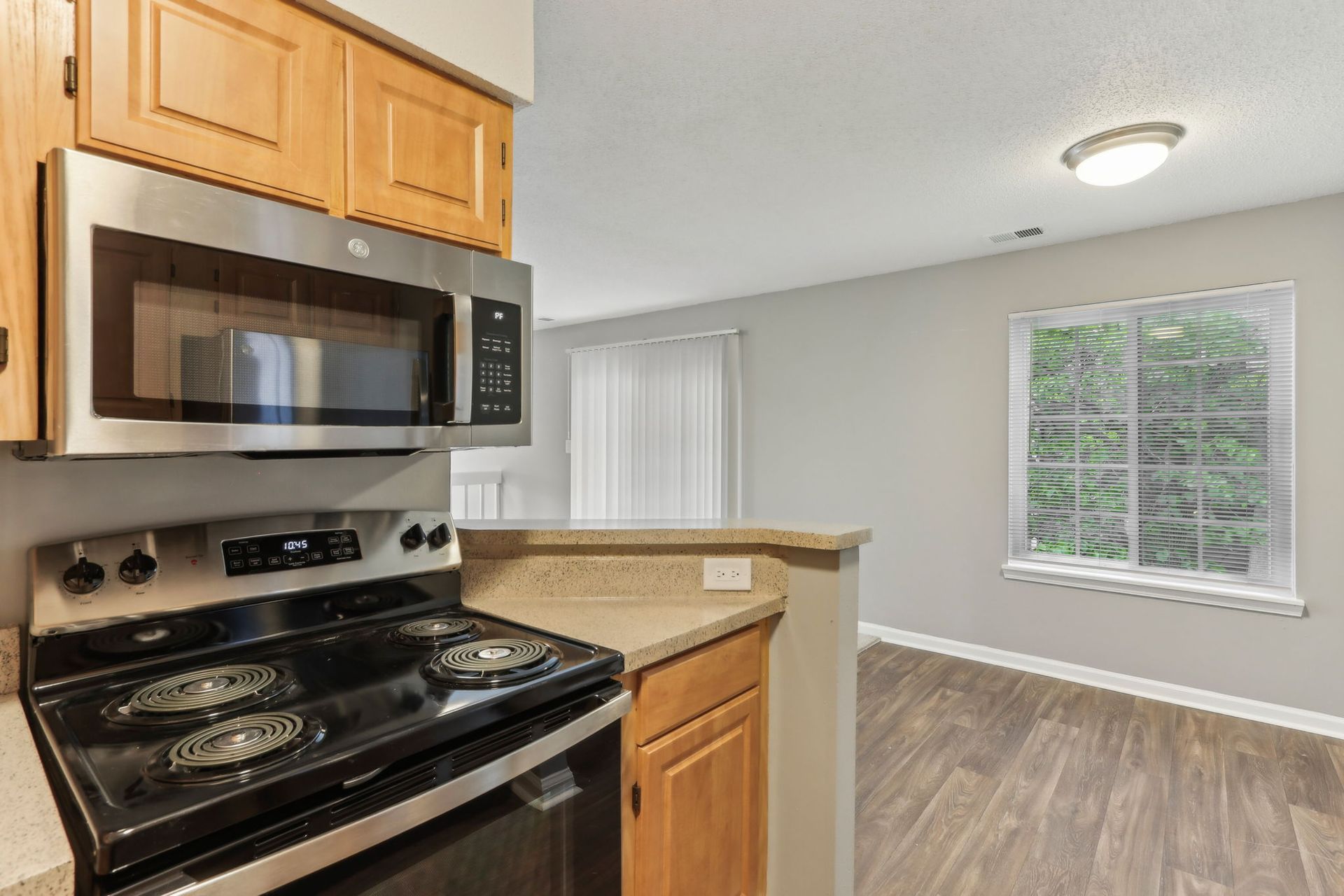 Kitchen with light wood cabinets, stainless steel appliances, and a window overlooking trees.