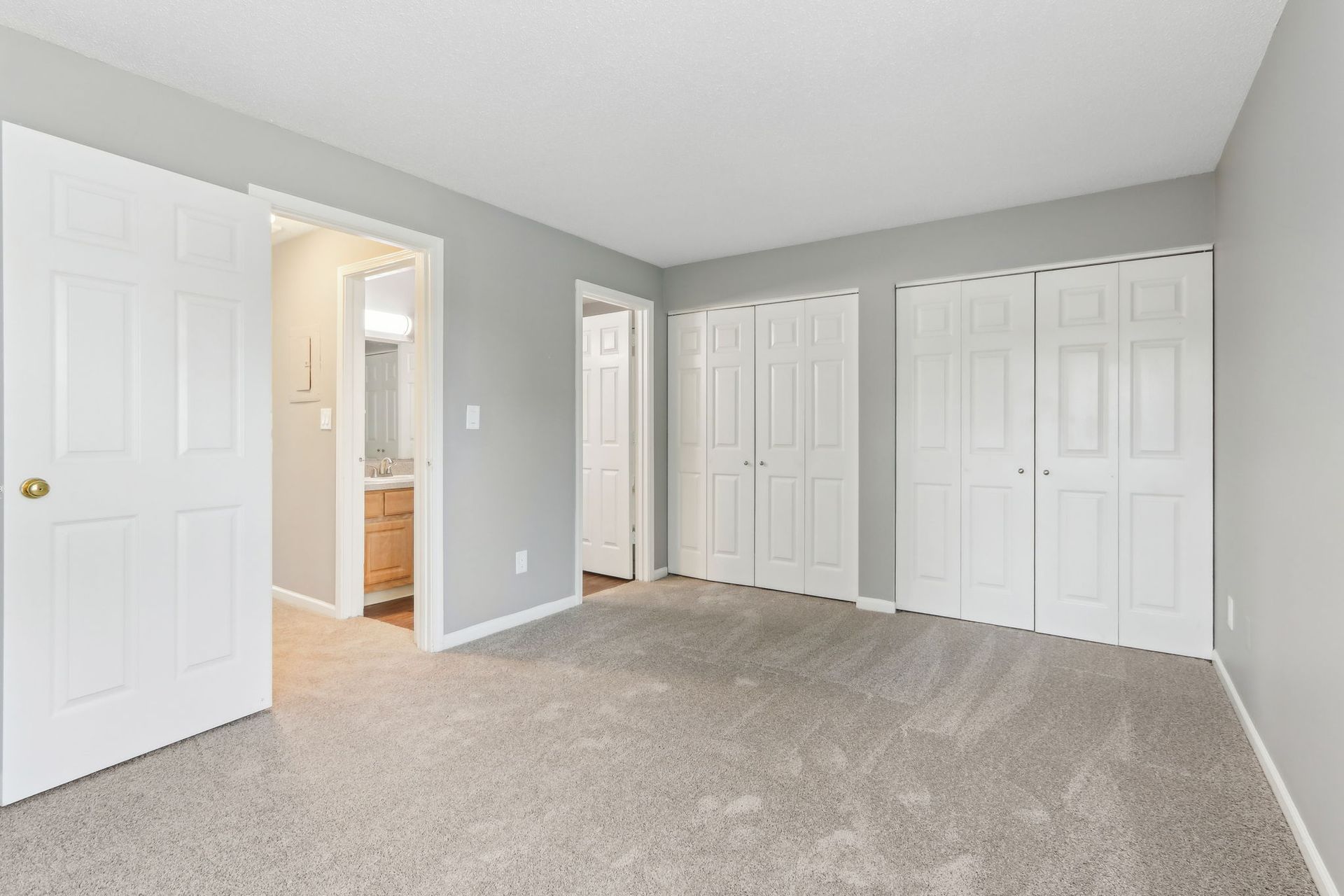 Bedroom with gray walls, white doors, carpet, and a doorway to a bathroom.
