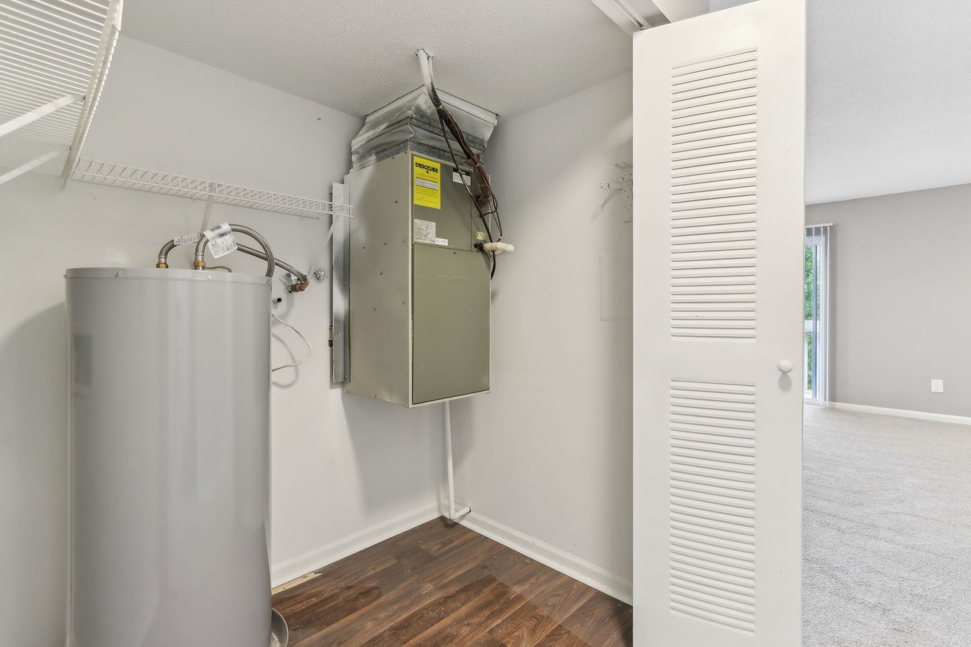 A utility closet with a water heater and air conditioning unit next to a closed, slatted door.