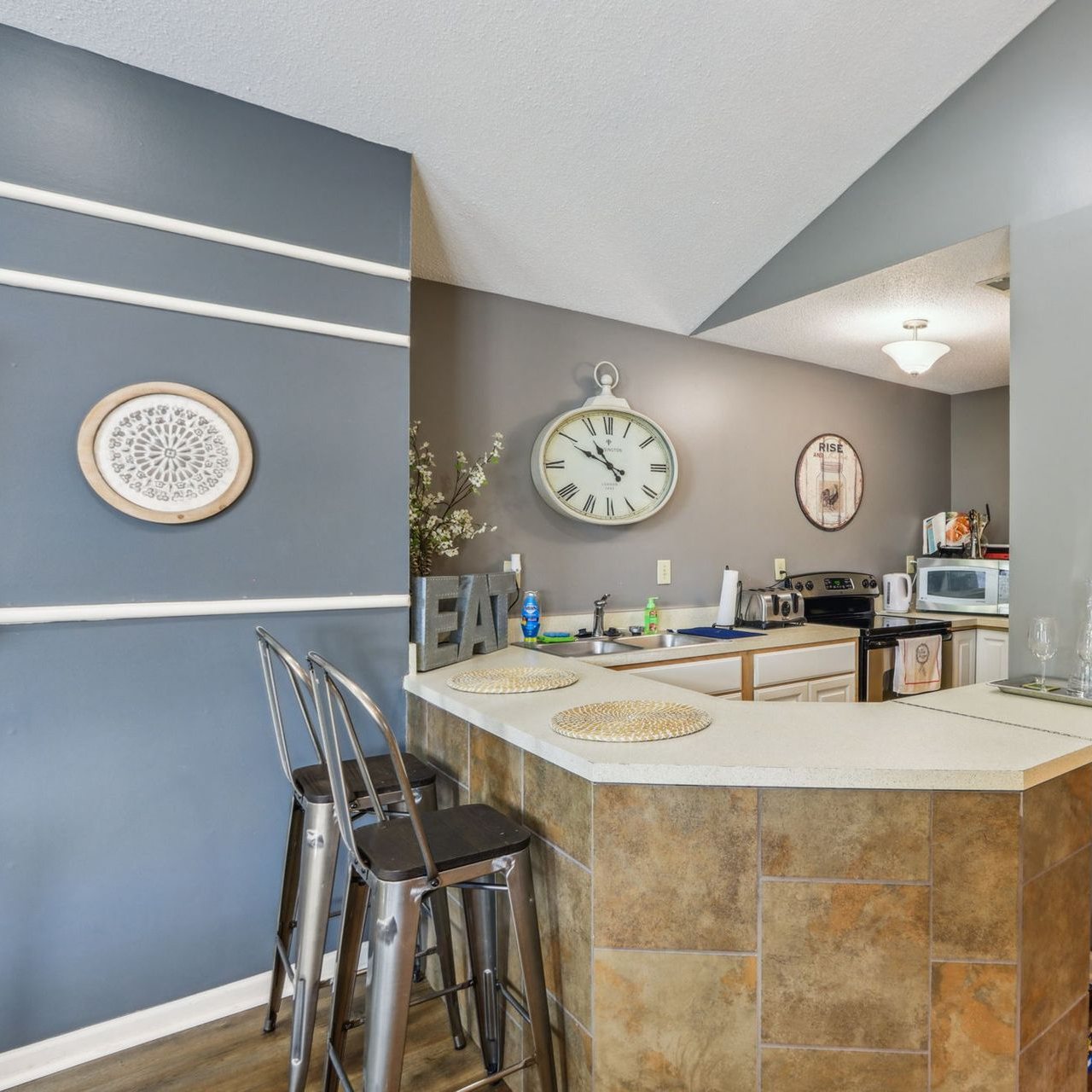 Kitchen with gray walls, bar seating, and a large clock.