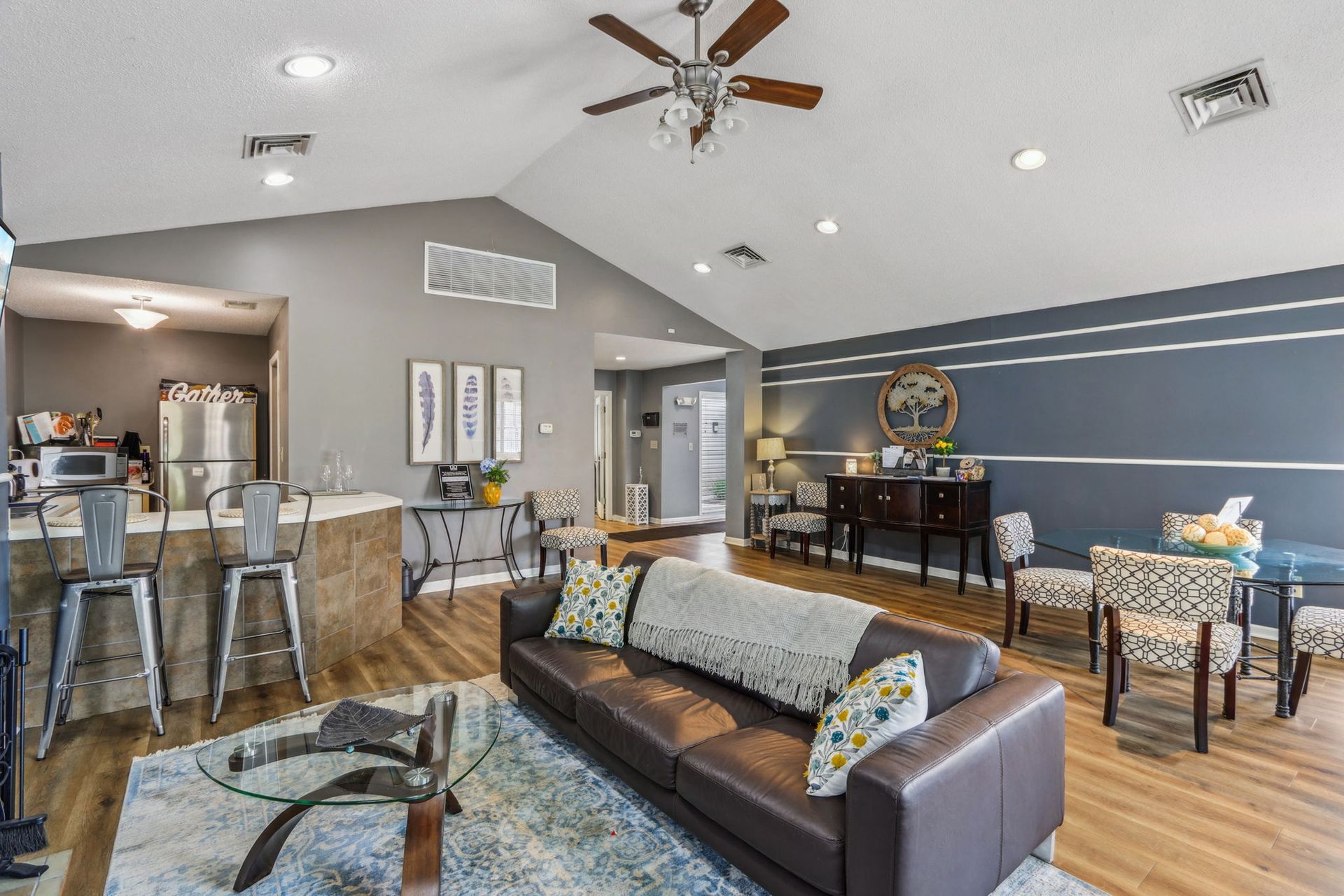 Spacious living room with brown leather sofa, dining area, and kitchen with bar stools.