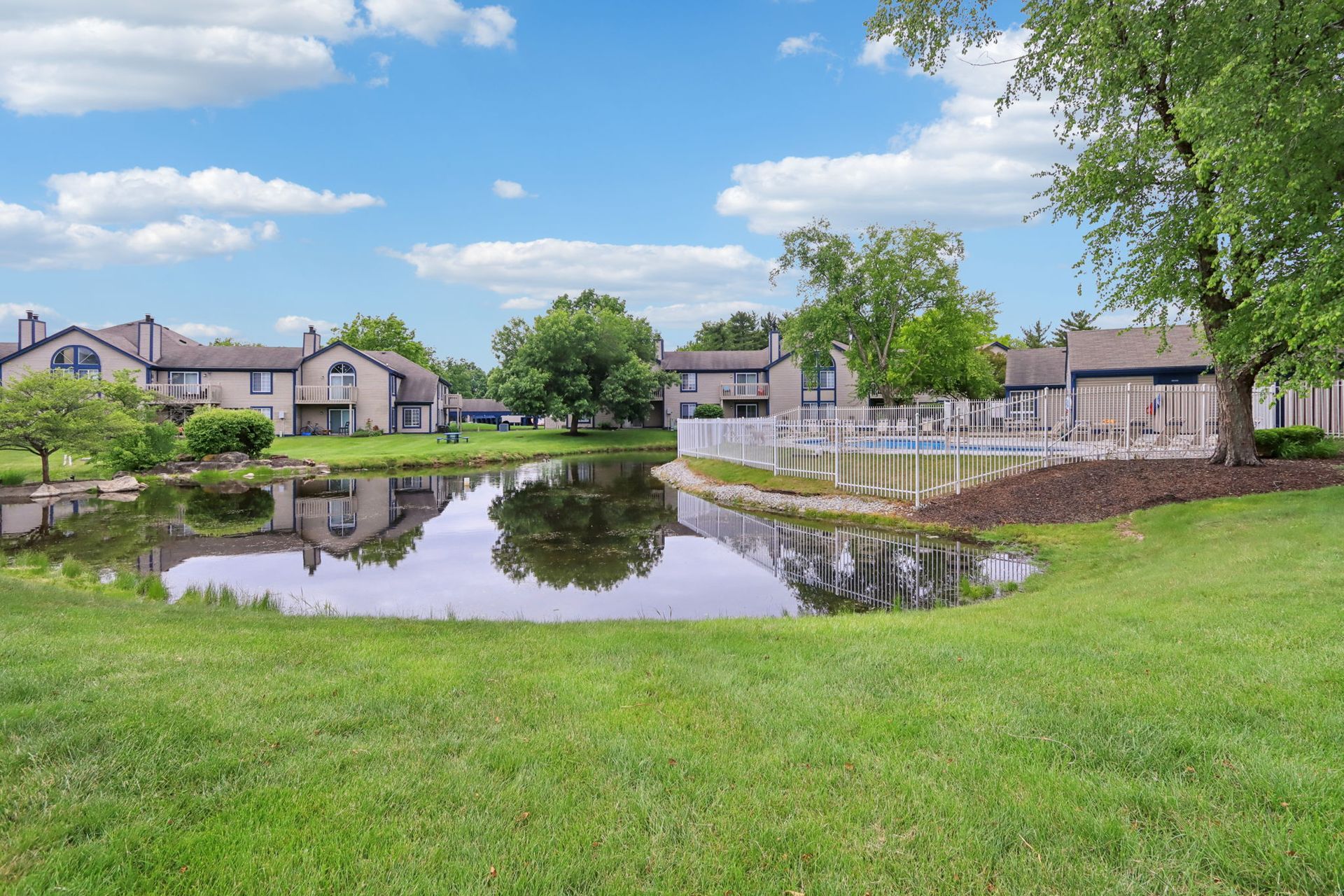 Pond in front of apartments, with blue sky and green grass.