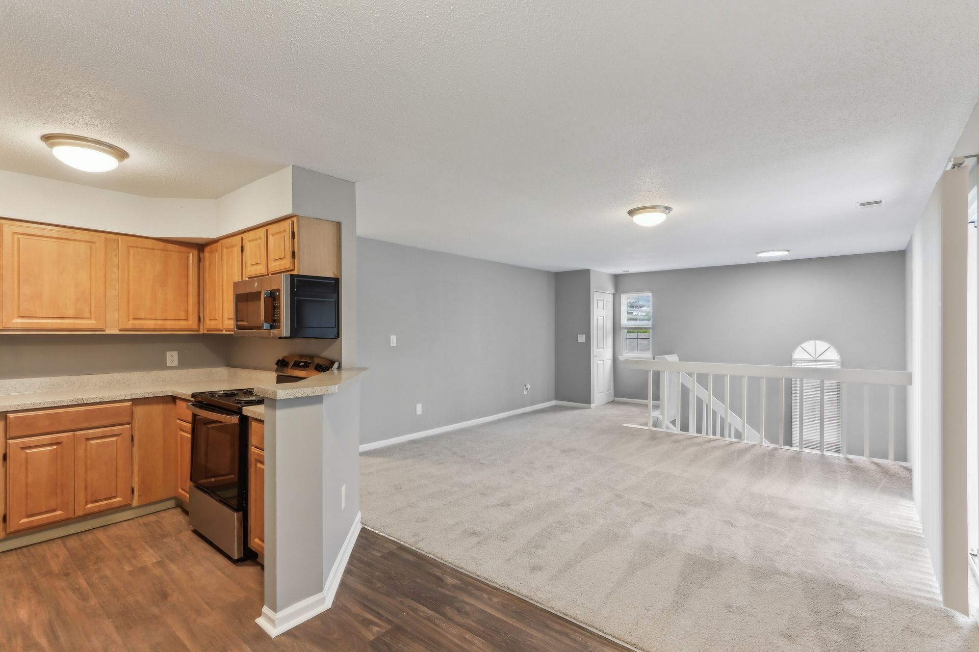 Kitchen with wood cabinets, stainless steel appliances, carpeted living area, and a staircase.