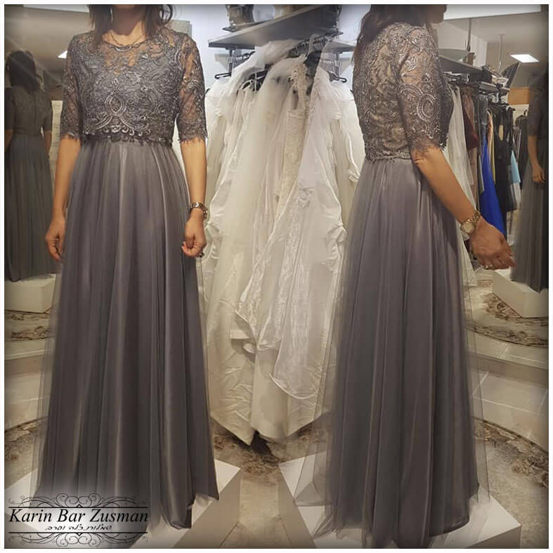 אישה בשמלה רשמית ארוכה אפורה עם חלק עליון תחרה; עומדת בחנות עם שמלות.