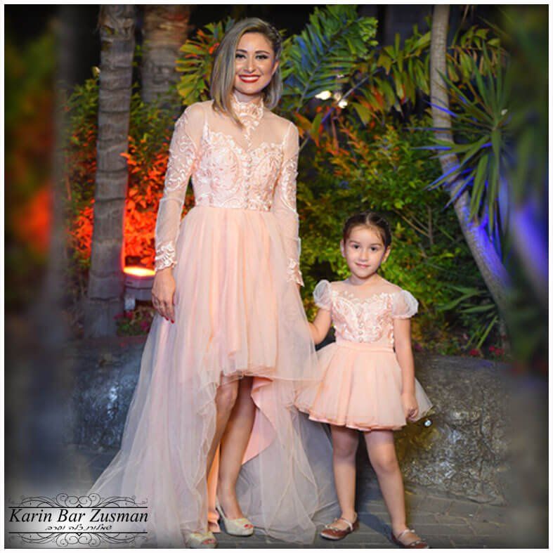 אישה וילדה בשמלות אפרסק תואמות, בחוץ. לשמלה של האישה שובל ארוך. שתיהן מחייכות.